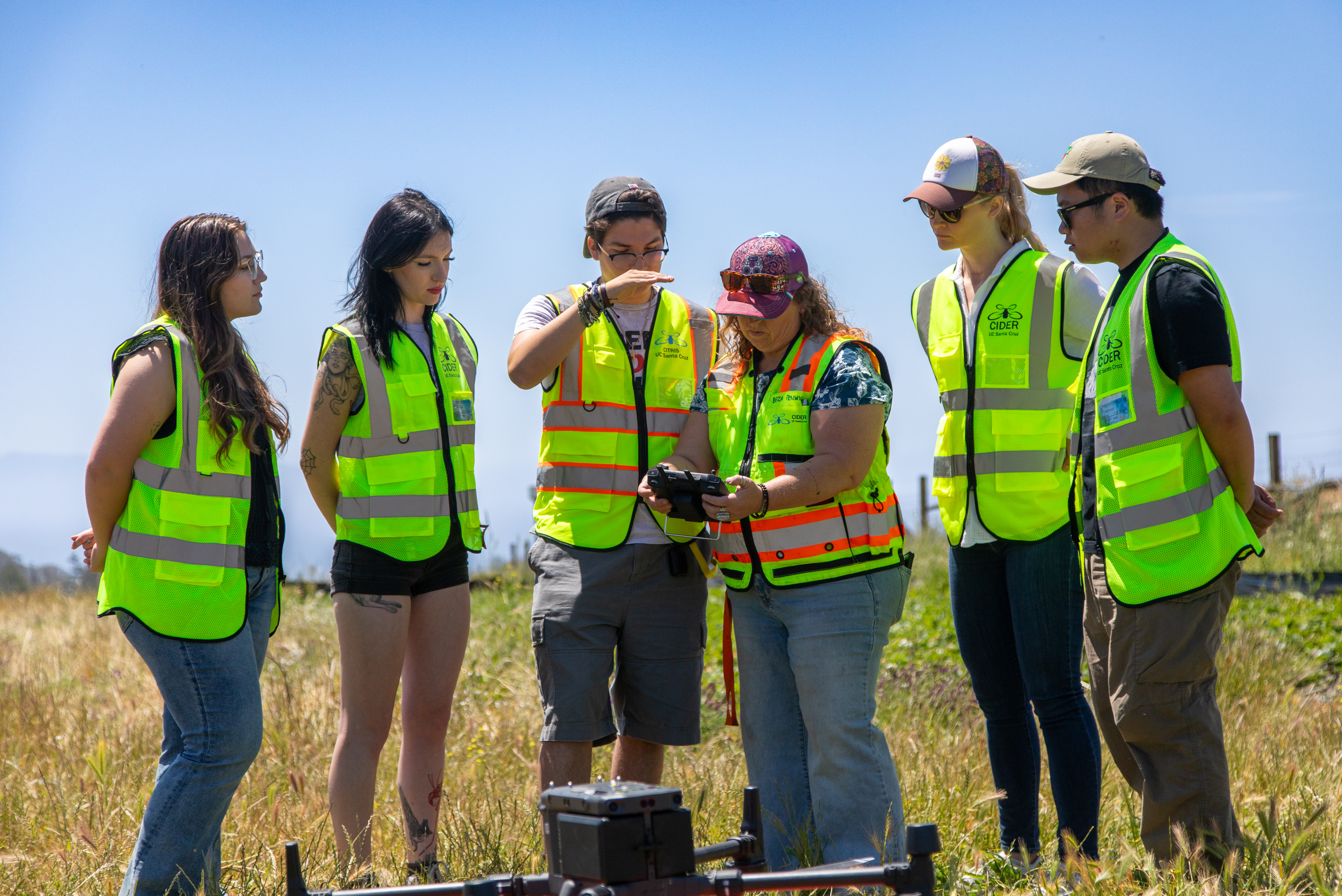 six people in safety vests look at a drone operating system